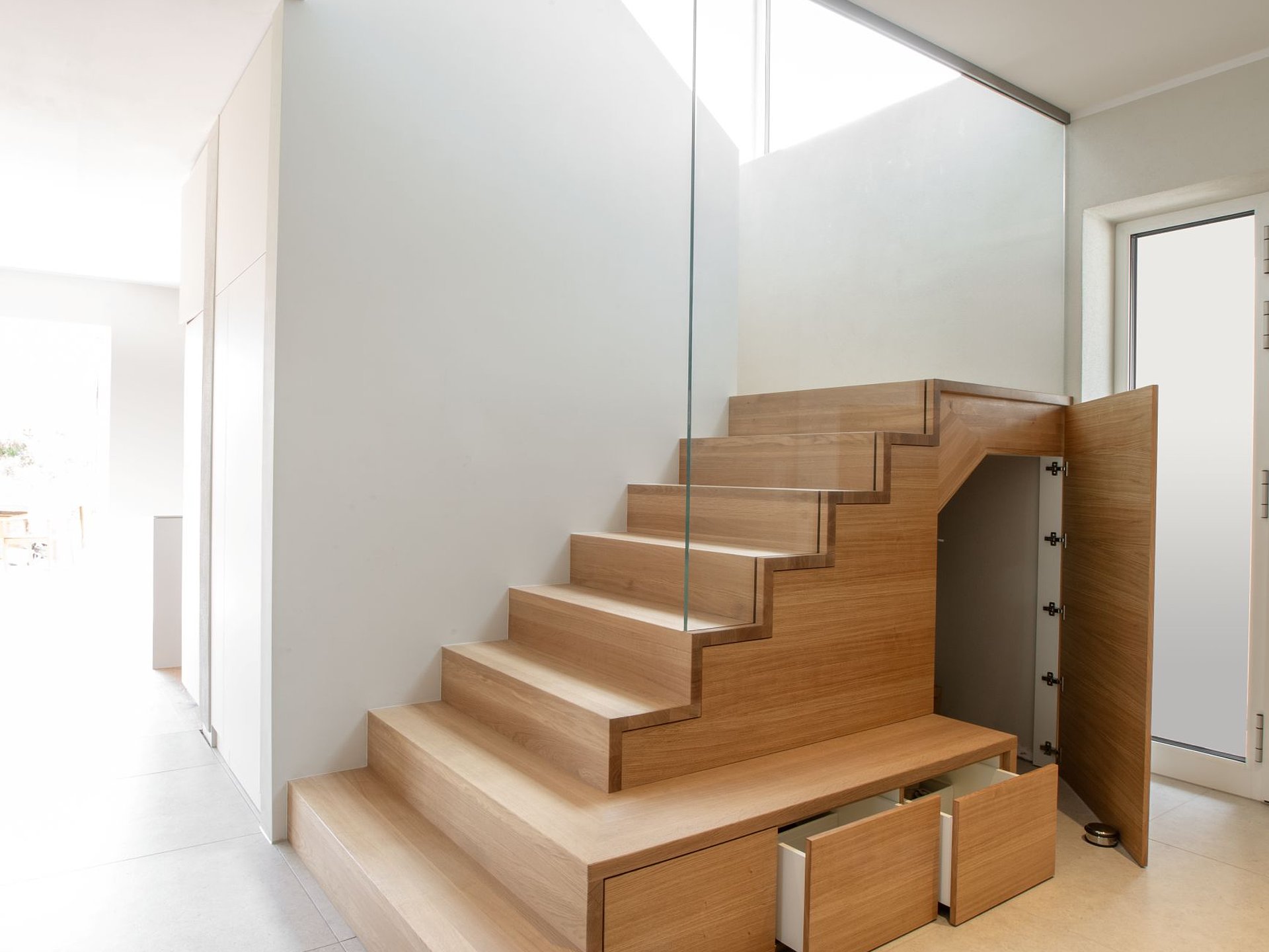 Geöffneter Treppenschrank unter einer Holztreppe mit mehreren Schubladen und einem großen seitlichen Schrankfach als individuell integriertem Stauraum.