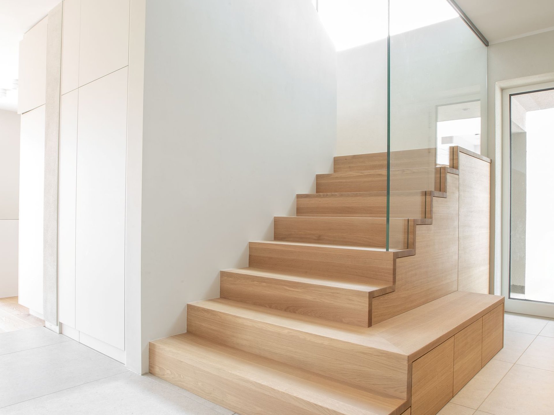 Individuell gefertigte Schranktreppe mit Holzstufen, integriertem Stauraum im Treppenunterbau und transparentem Glasgeländer.