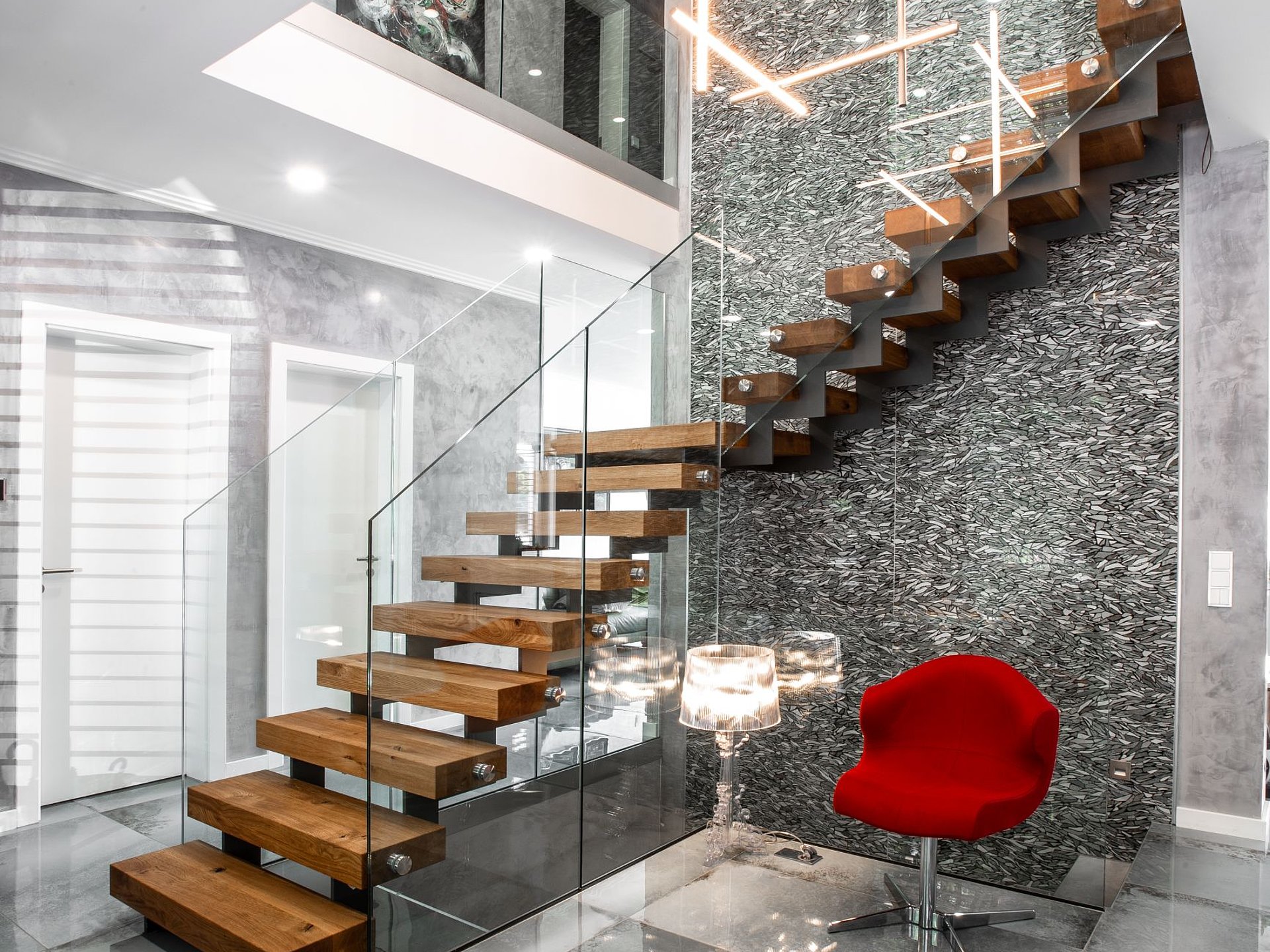 Stahl-Holz-Treppe mit Glasgeländer im Wohnhaus Moderne Stahl-Holz-Treppe mit anthrazitfarbener Zickzackwange, massiven Eichenstufen und rahmenlosem Glasgeländer. Die Treppe bildet den architektonischen Mittelpunkt eines offen gestalteten Wohnbereichs.