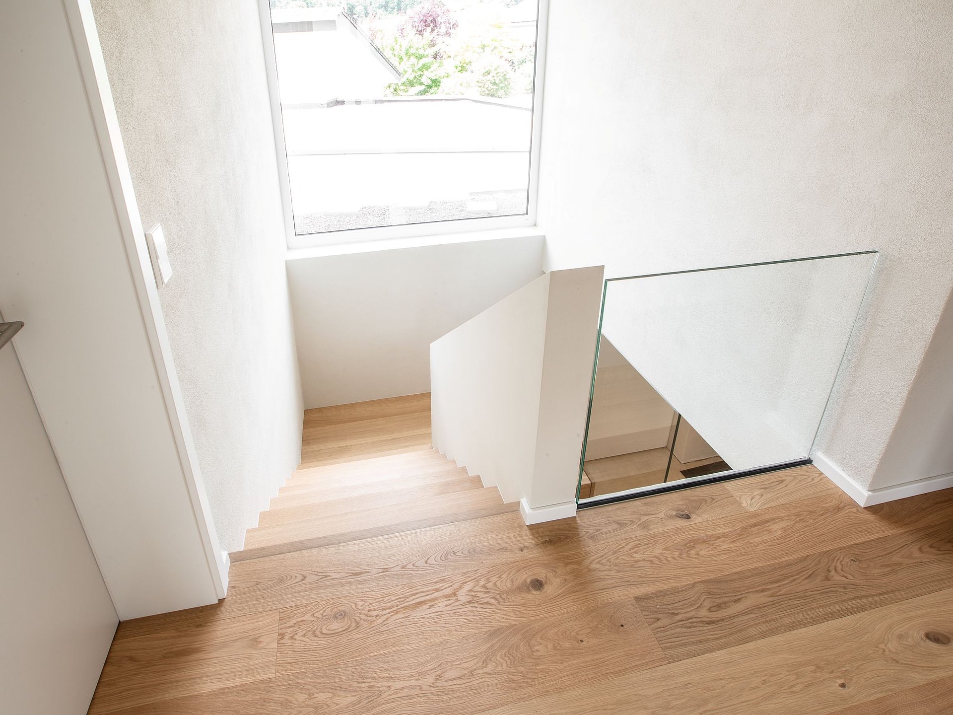 Glasgeländer am Austritt einer Holztreppe Rahmenlos wirkendes Glasgeländer am oberen Austritt einer Holztreppe. Die transparente Glasscheibe sichert die offene Seite des Treppenhauses, ohne den hellen Raum optisch zu schließen.