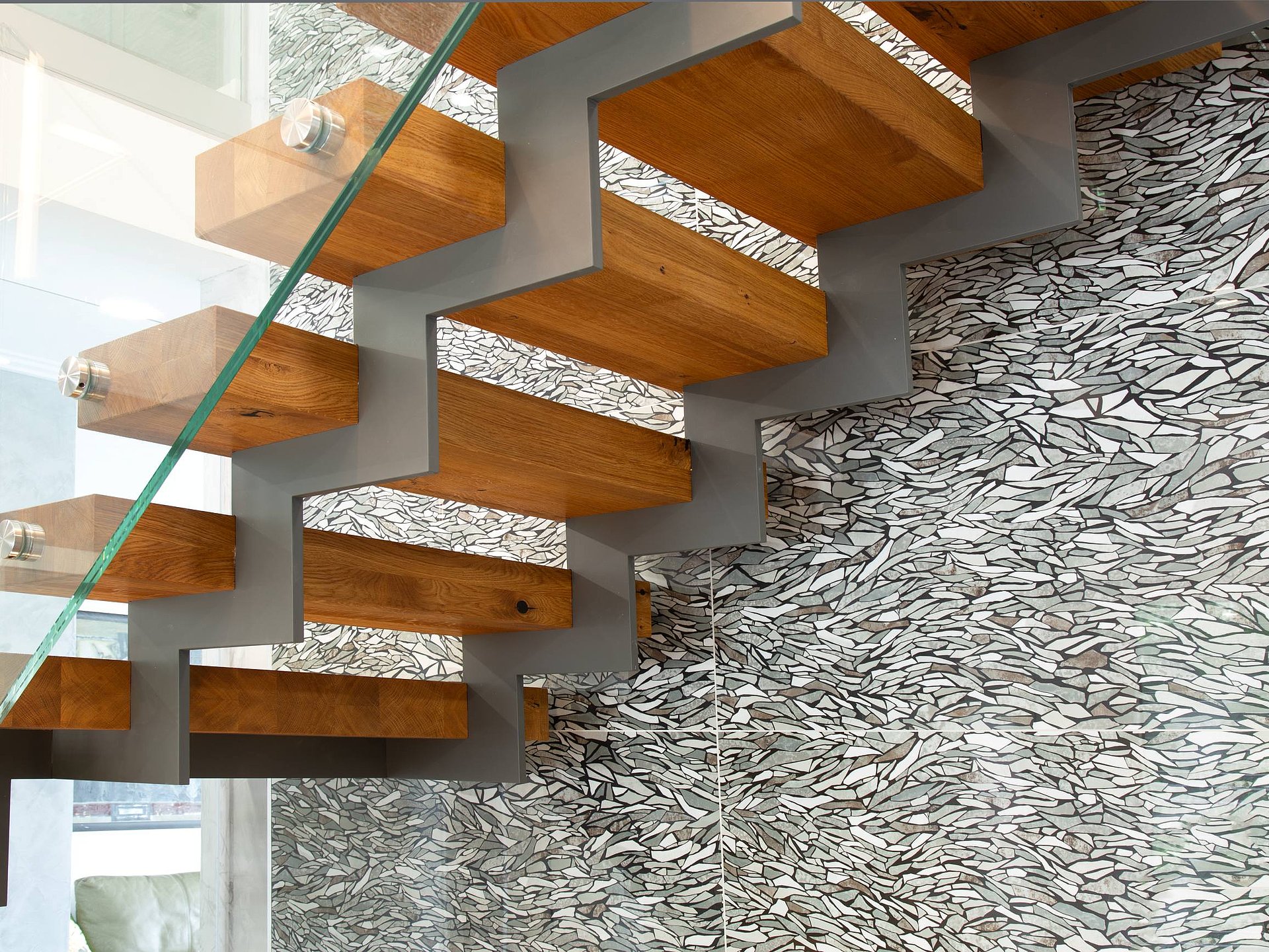 Detail einer Stahl-Holz-Treppe mit Zickzackwange Detailaufnahme einer Stahl-Holz-Treppe mit anthrazitfarbener Zickzackwange, massiven Eichenstufen und Glasgeländer. Die Aufnahme hebt die präzise Verarbeitung und das markante Tragwerk hervor.