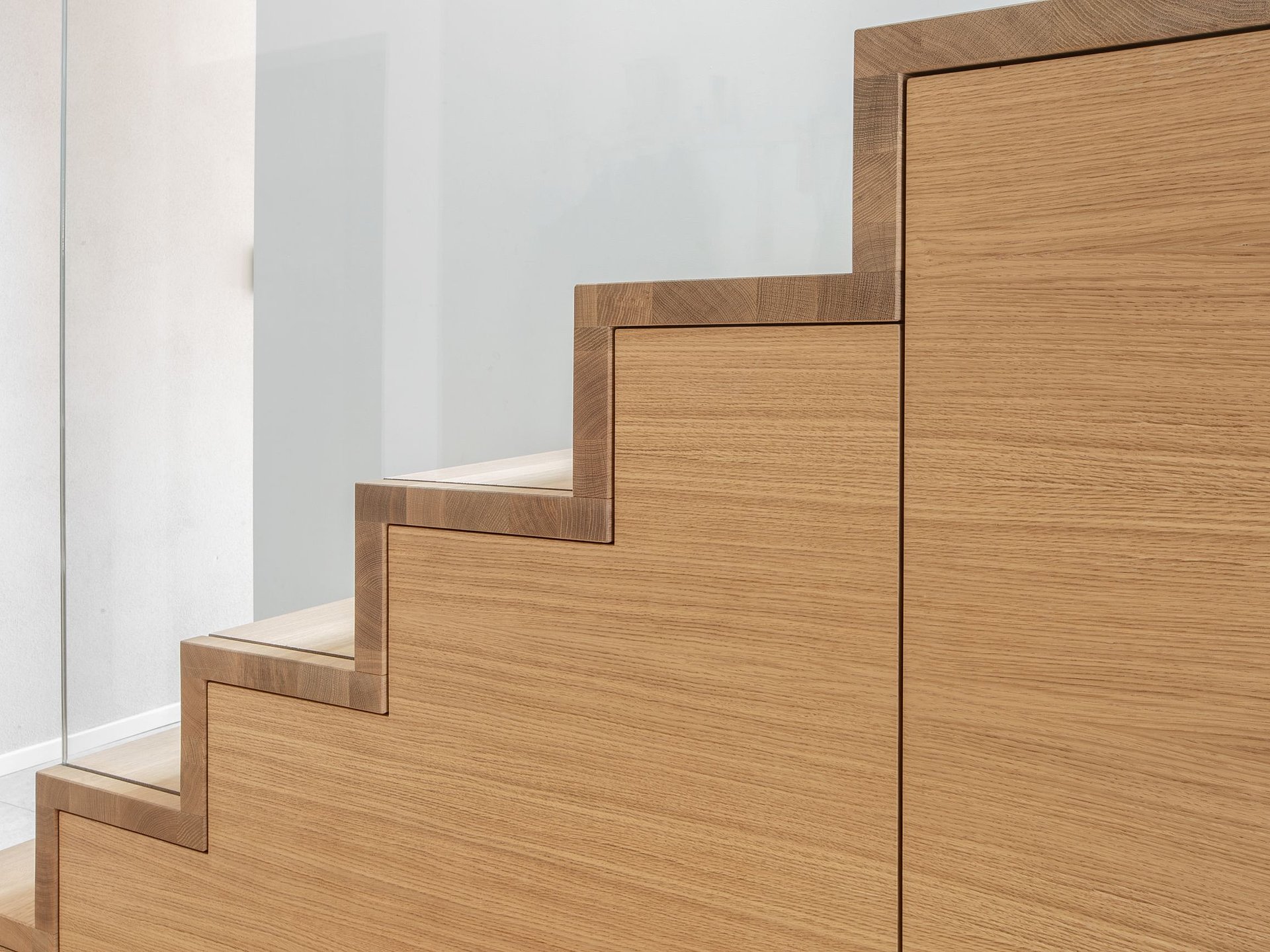 Detailansicht der passgenauen Holzverkleidung eines Treppenschranks mit stufenförmig angeordneten Schrankfronten unter der Treppe.
