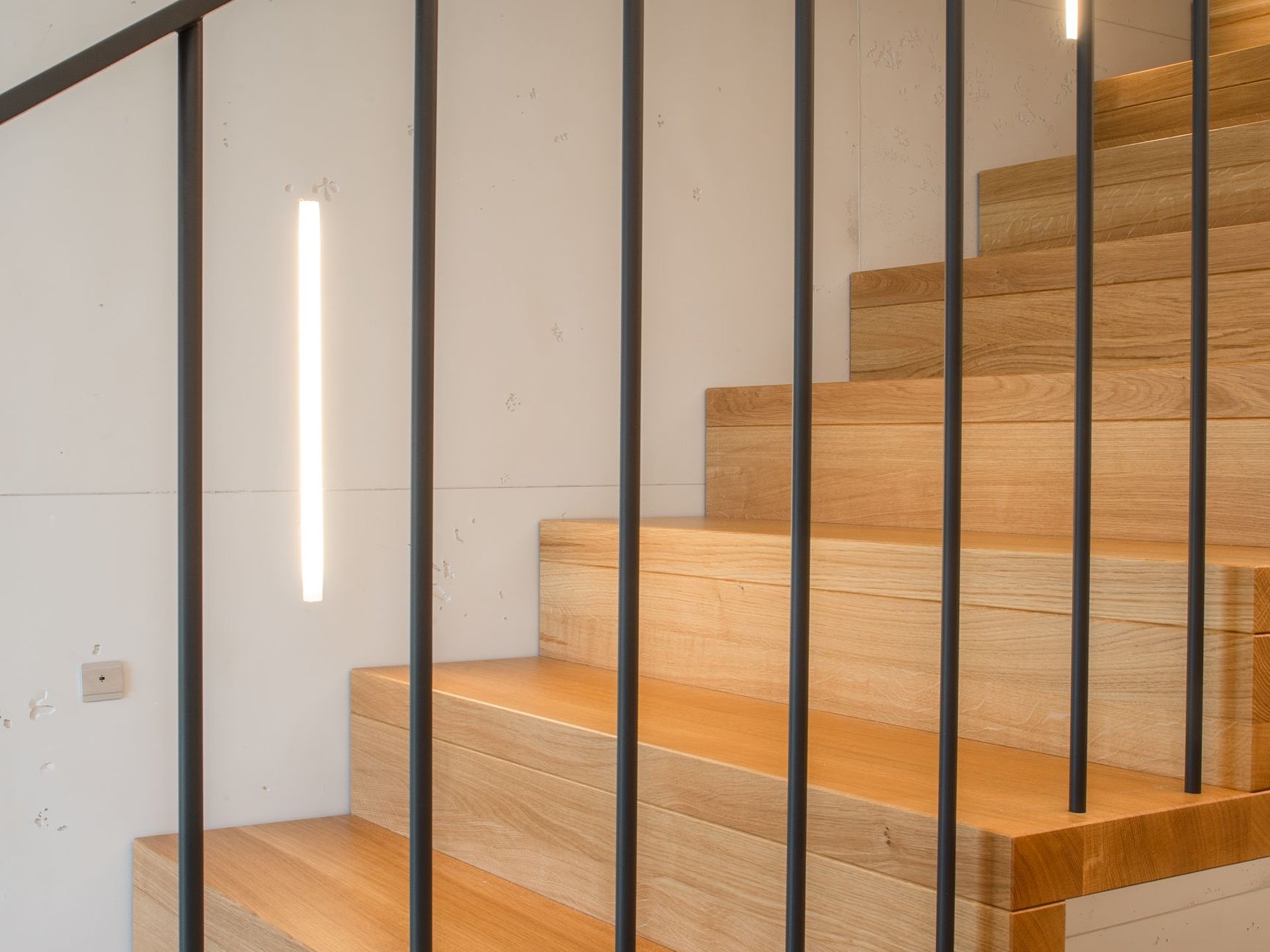 Detailansicht einer Faltwerktreppe aus Eichenholz mit senkrechten, anthrazitfarbenen Stahlstaketen. Im Fokus stehen die klaren Übergänge zwischen Tritt- und Setzstufen.