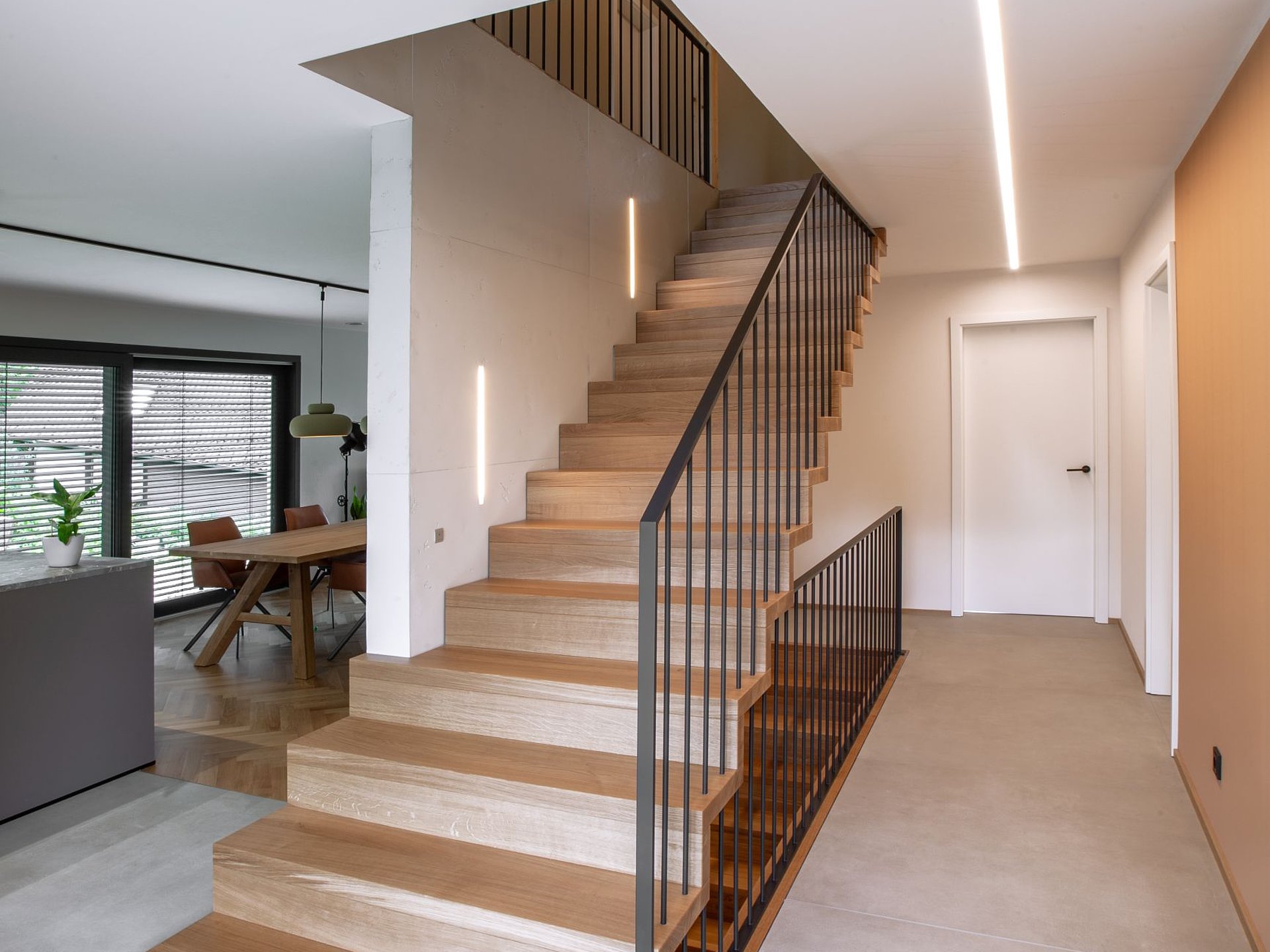 Geradläufige Faltwerktreppe aus hellem Holz mit schlankem Stahlgeländer. Die durchgängige Faltung von Tritt- und Setzstufen prägt die geradlinige Gestaltung des Treppenhauses.