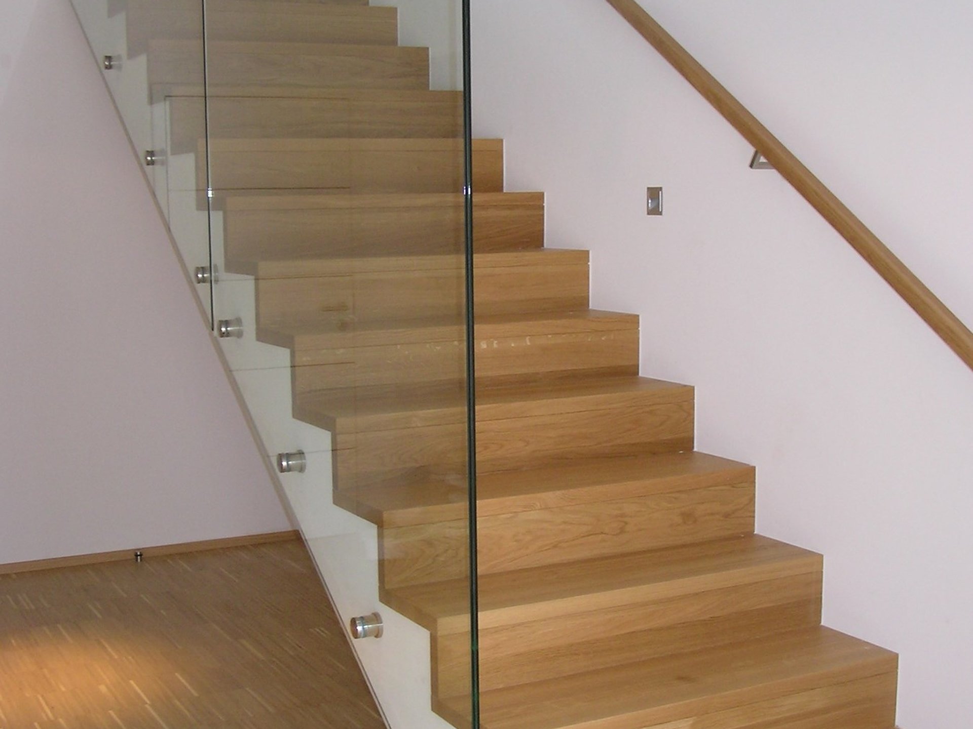Treppe mit Faltwerkbelag aus Holz mit Glasgeländer und Wandhandlauf