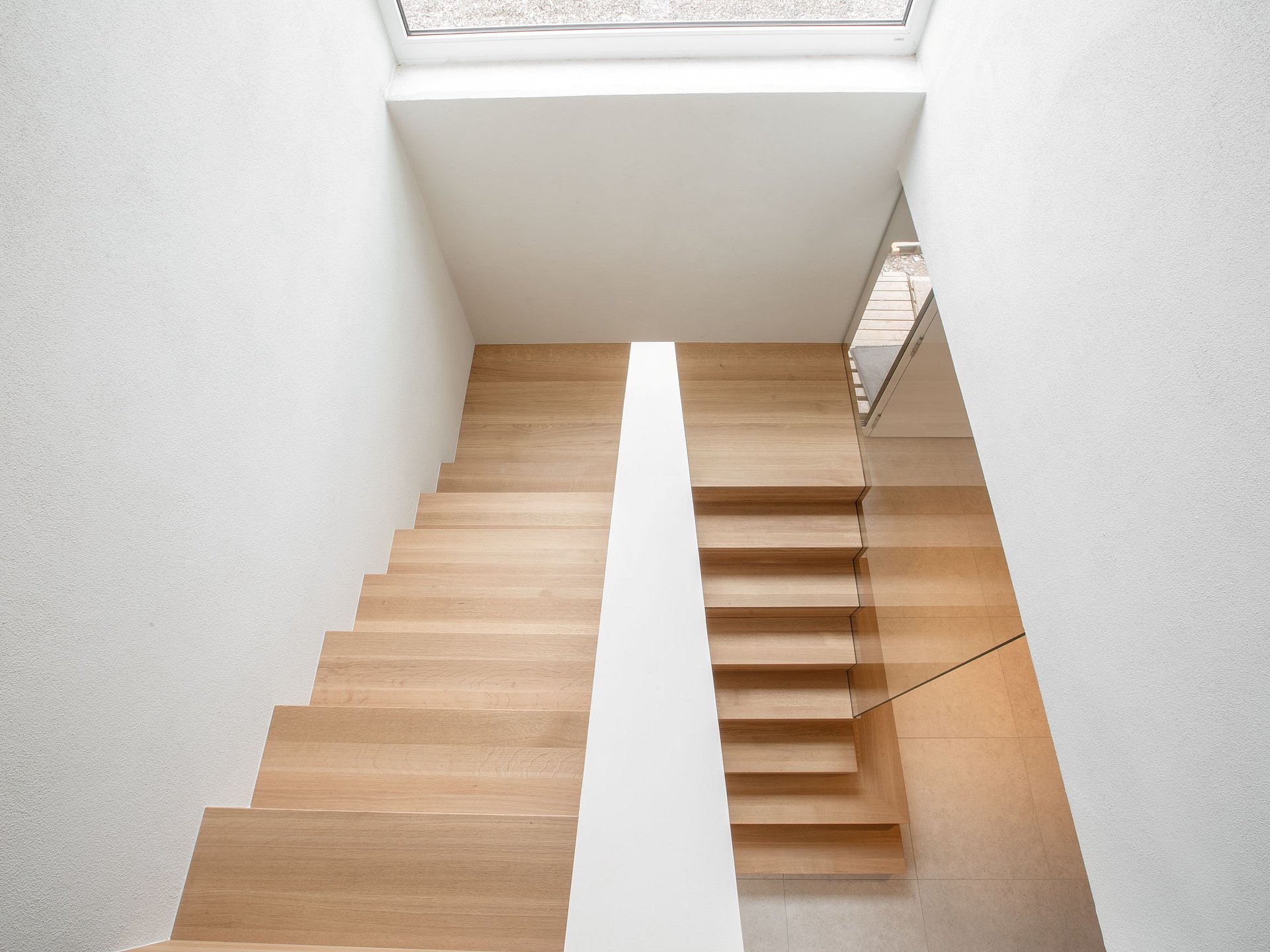 Betontreppe mit Holzstufen und Glasgeländer Blick von oben auf eine Betontreppe mit hellen Holzstufen und transparentem Glasgeländer. Die geradlinige Gestaltung fügt sich in den hellen, modern gestalteten Treppenraum ein.