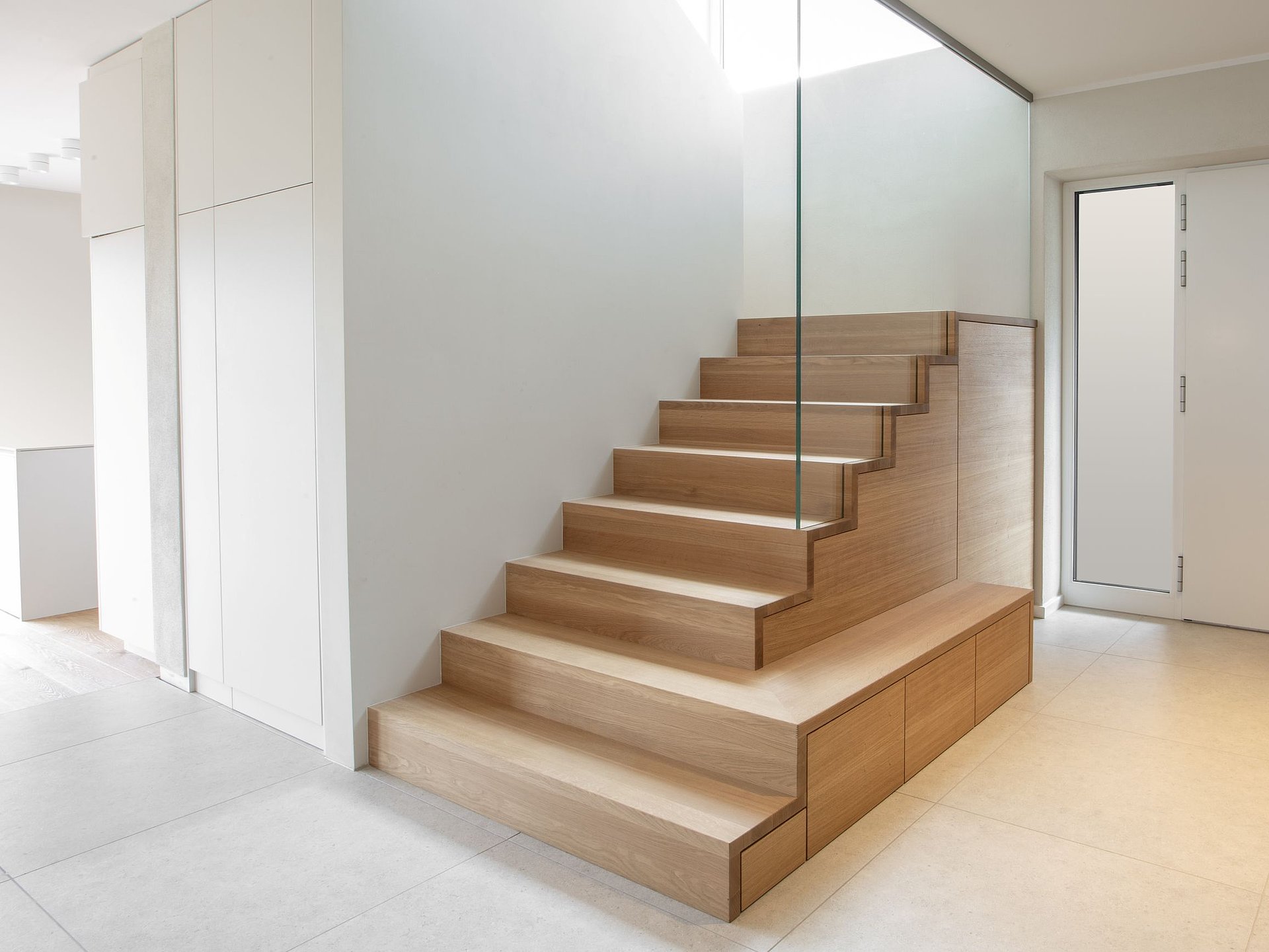 Maßgefertigte Schranktreppe aus Holz mit geschlossenem Treppenschrank und Schubladen unter den Stufen sowie einem seitlichen Glasgeländer.