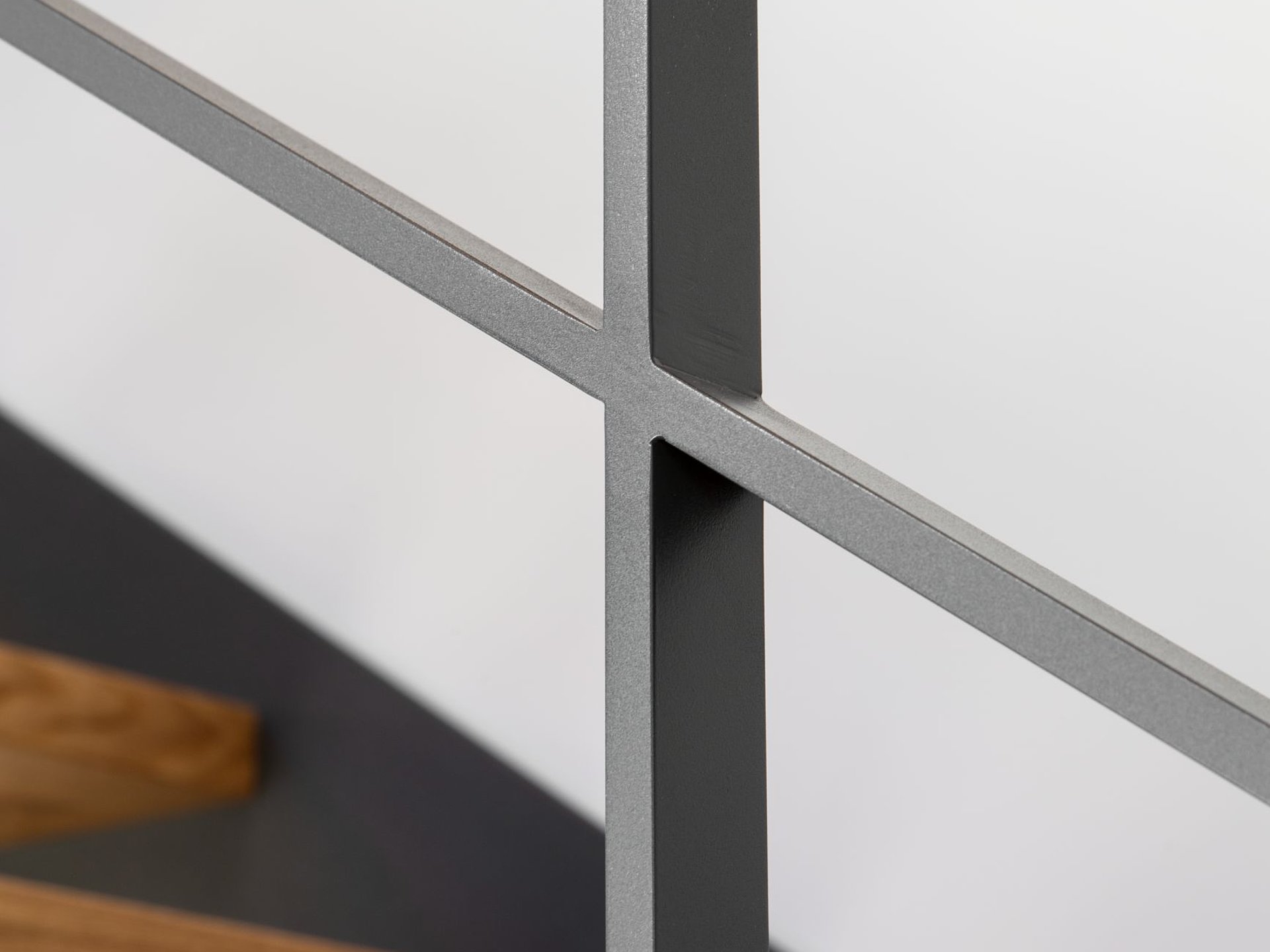 Detail einer Stahlgeländer-Verbindung Nahaufnahme der präzise ausgeführten Verbindung eines anthrazitfarbenen Stahlgeländers. Im Hintergrund sind die Holzstufen der Treppe zu erkennen.